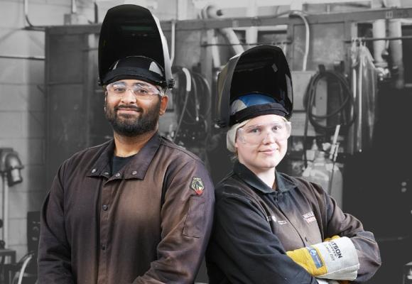 two students standing back-to-back in welding attire