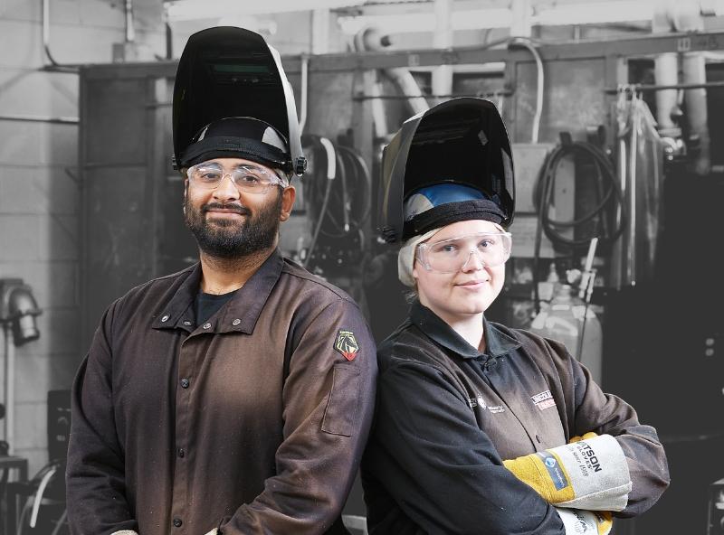 two students standing back-to-back in welding attire